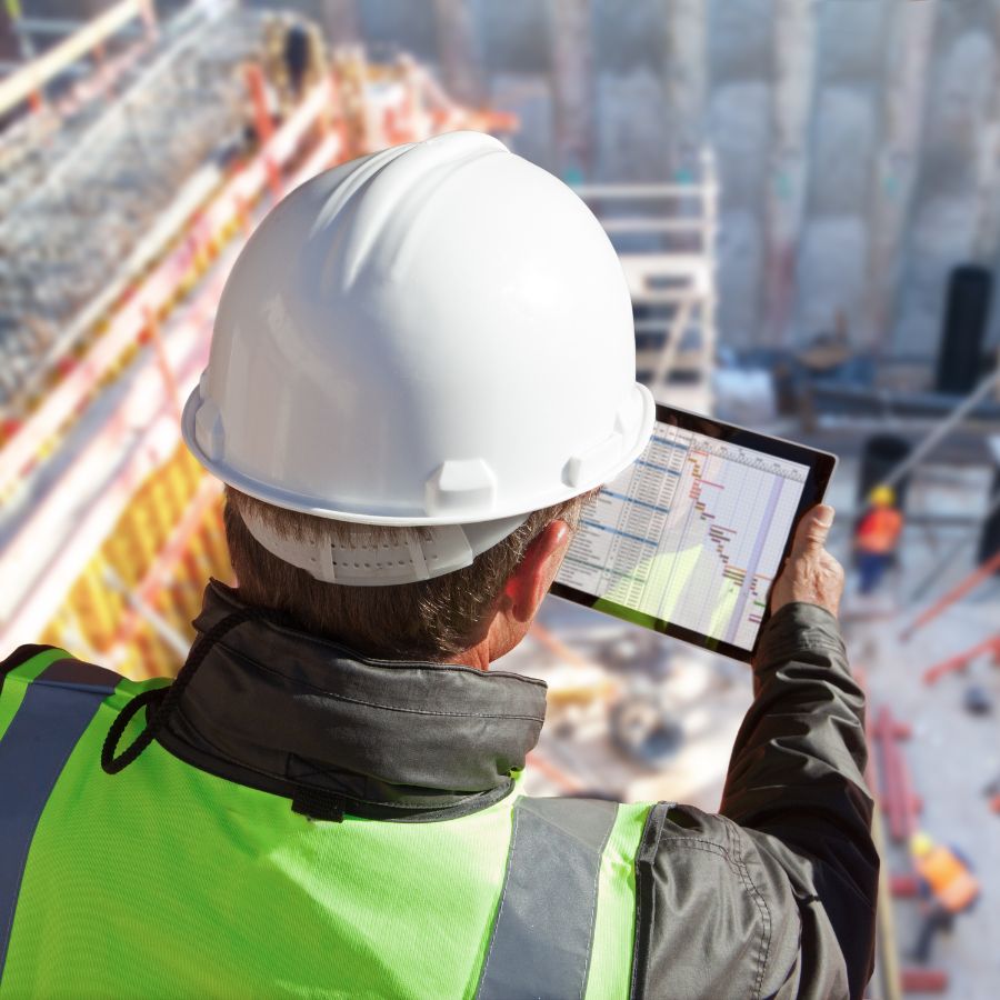 Construction worker looking down at tablet at the top of a building analyzing Cybersecurity for Construction